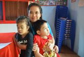 A woman embraces two children, a boy and a girl. Latsaphone, a teacher trained by HI who works with children like Junior, aged 8 (right) in a transitional class in Champassak province, Laos.  