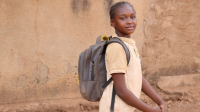 Portrait of Perpétue in profile, looking at the camera and smiling. She is carrying a school rucksack on her back.