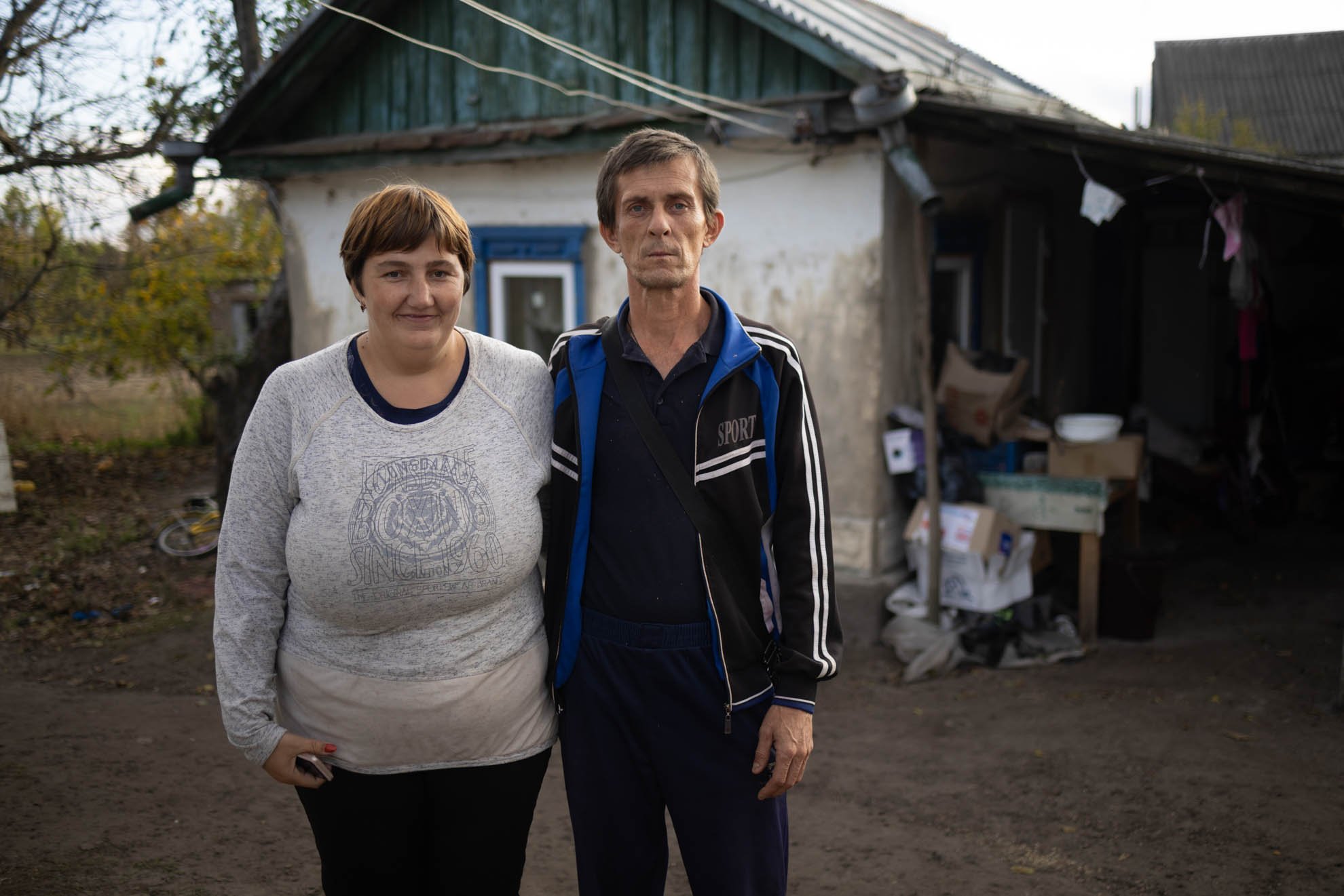 Olha and Volodymyr are standing outside their house. Olha is smiling.