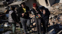 People walk in front of a collapsed building with a wounded person